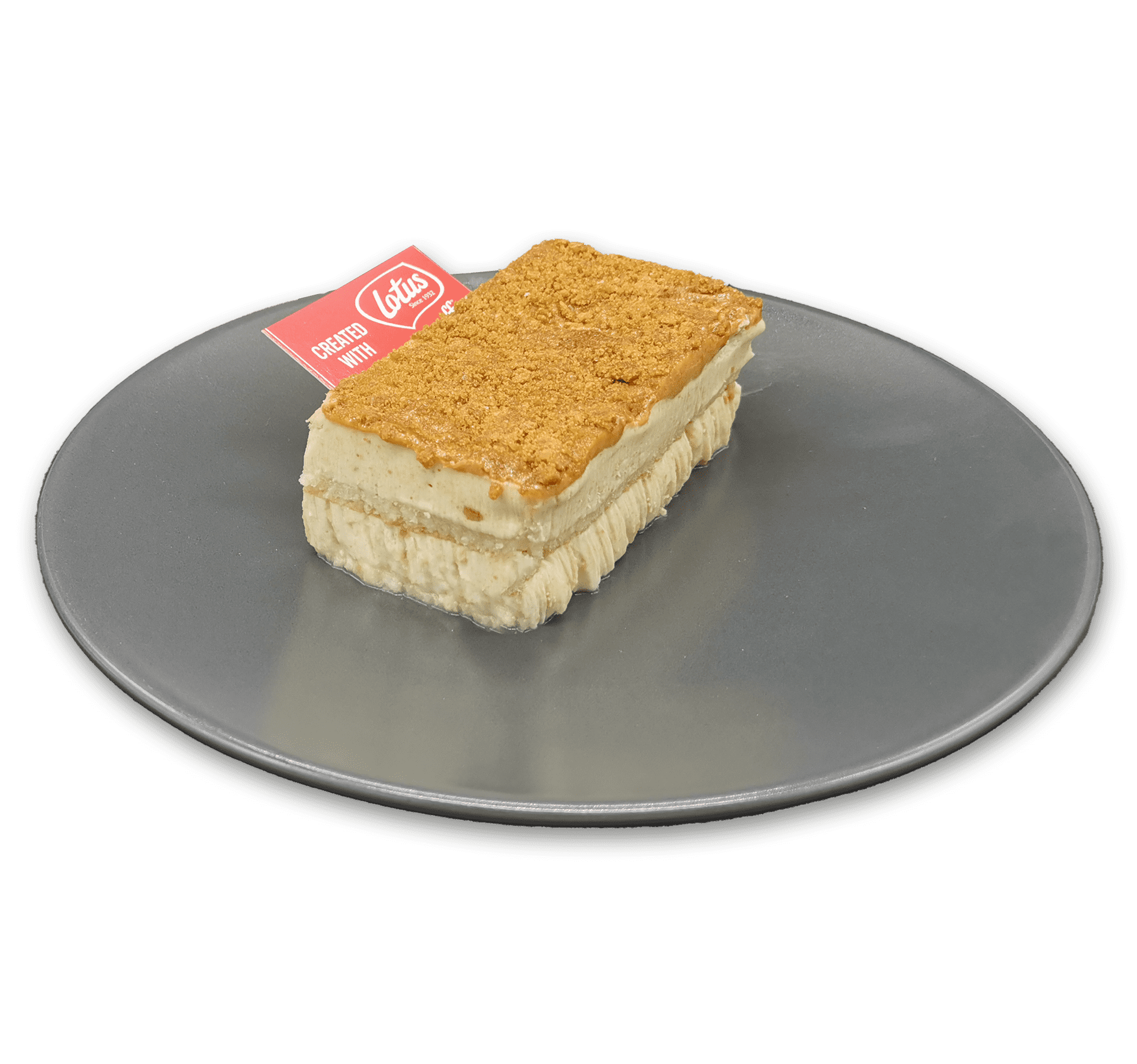 Una tarta Lotus rectangular con una cobertura desmenuzable reposa sobre un plato gris. El postre, elaborado con capas de bizcocho y crema, se parece al popular sabor Lotus. En la capa superior hay insertada una pequeña etiqueta roja y blanca.