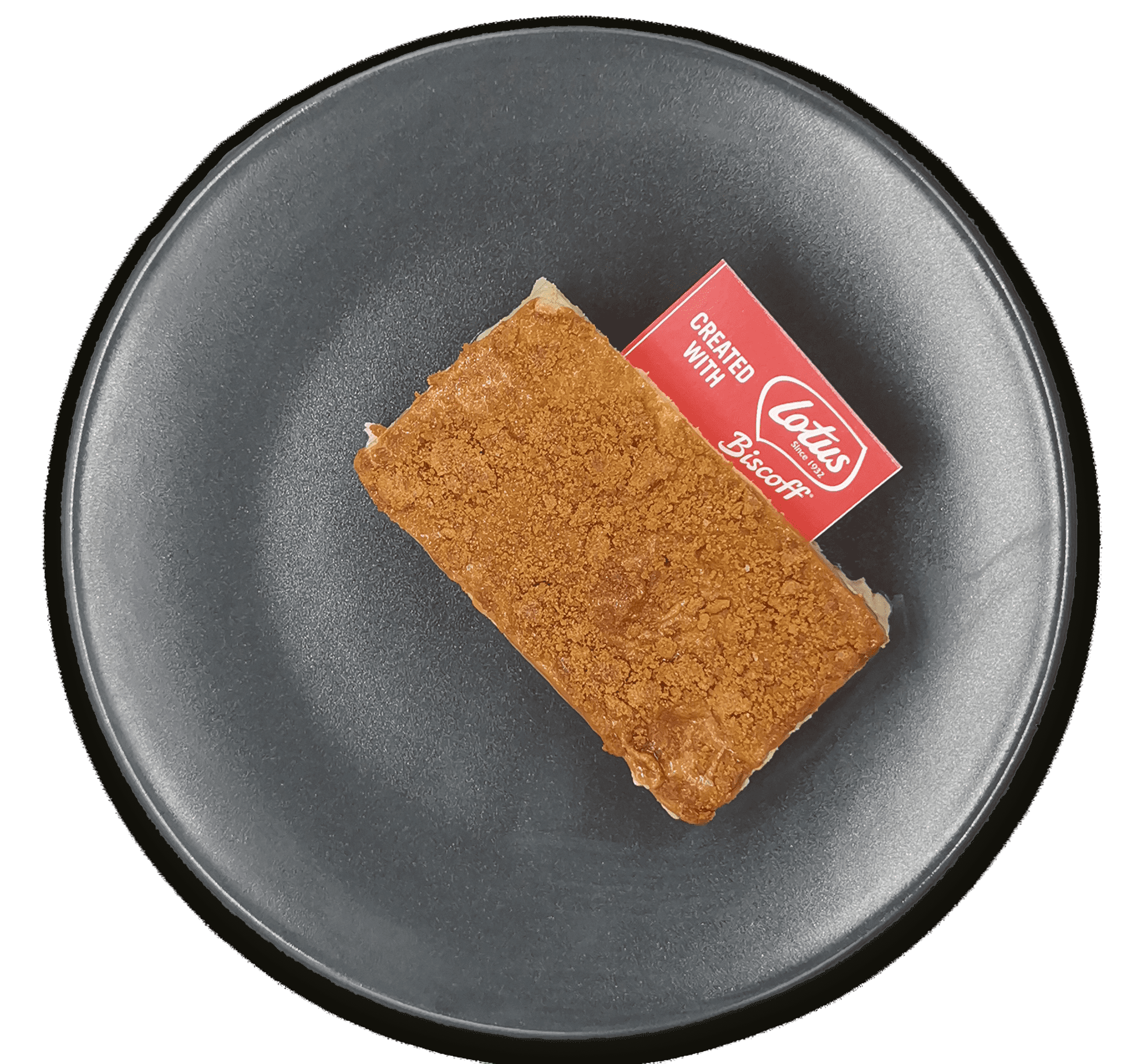 Un postre rectangular de Tarta Lotus, con sabor a Biscoff, reposa sobre un plato negro. Está cubierto con una galleta Biscoff y un pequeño papel rojo que dice "Creado con Lotus Biscoff".